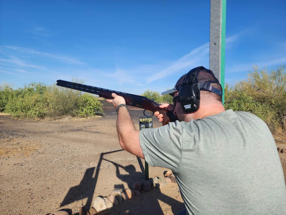 James B shouldering an over-under shotgun at a desert clay target range in Arizona
