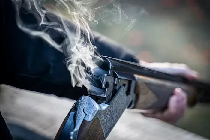 Close-up of an over-under shotgun broken open with smoke rising from the barrels