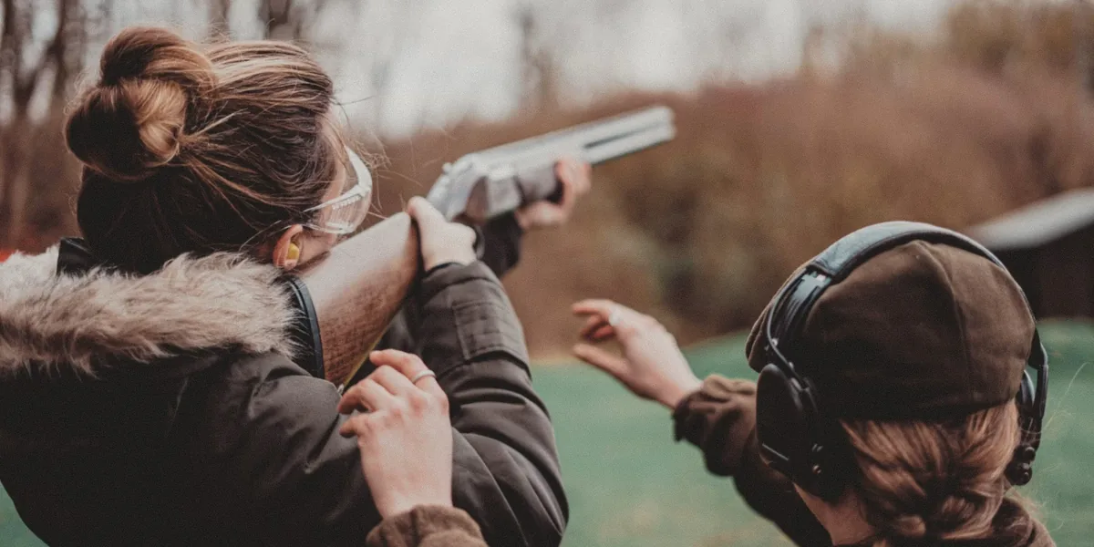 A new shooter aiming an over-under shotgun while an instructor points out the clay target